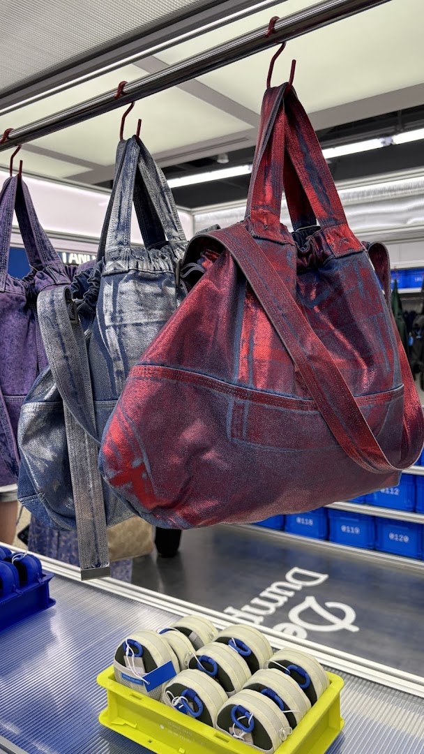 Colorful metallic-finish bags hang on display, with accessories in crates below, showcasing Beyond The Vines' unique designs.