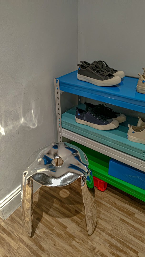 A unique silver stool sits beside colorful shelves displaying stylish sneakers in a modern retail space.