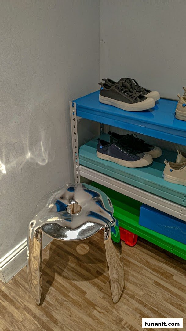 A unique silver stool sits beside colorful shelves displaying stylish sneakers in a modern retail space.