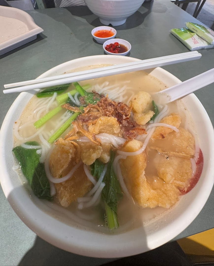 A close-up of a delicious bowl of noodles with crispy toppings and greens.