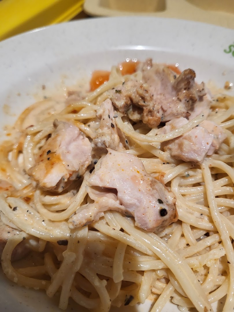 A close-up shot of creamy pasta with chicken pieces and cherry tomatoes in a white bowl.