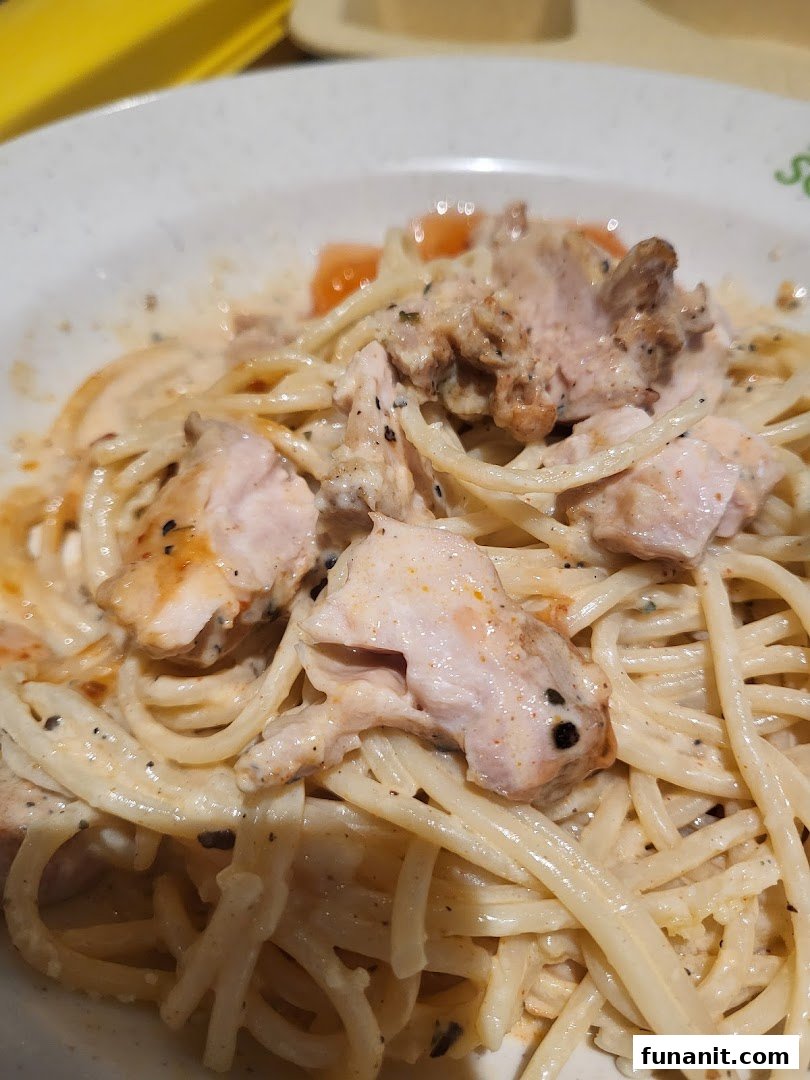 A close-up shot of creamy pasta with chicken pieces and cherry tomatoes in a white bowl.