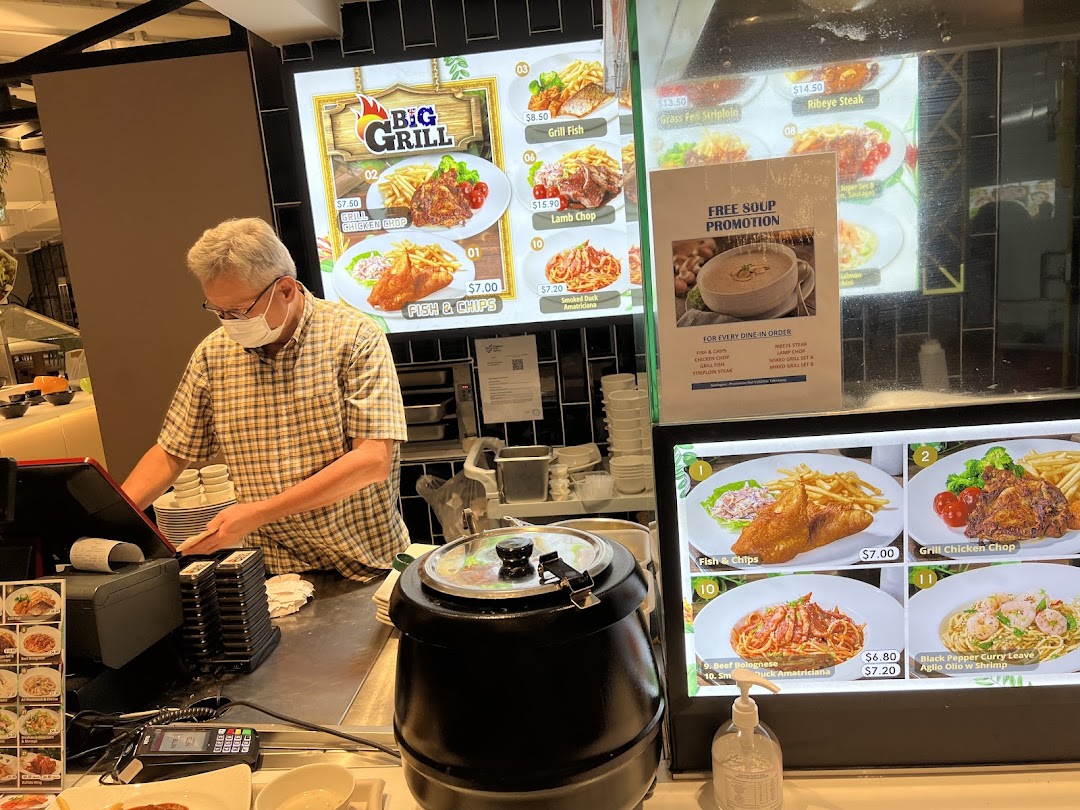 A staff member at Big Appetite's counter with digital menu boards displaying various grilled dishes and pasta.