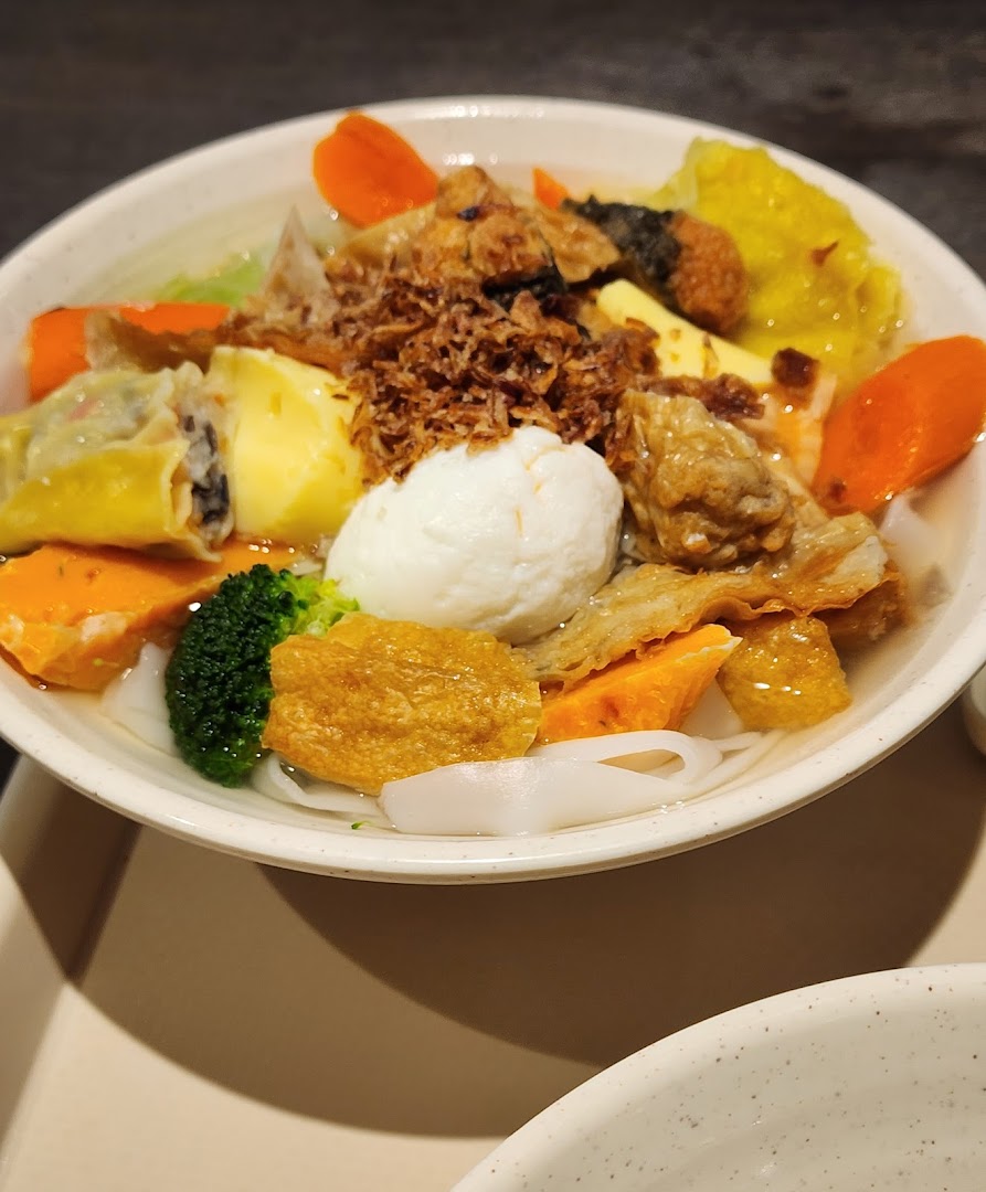 A vibrant bowl of noodle soup with fish balls, dumplings, vegetables, and fried toppings.