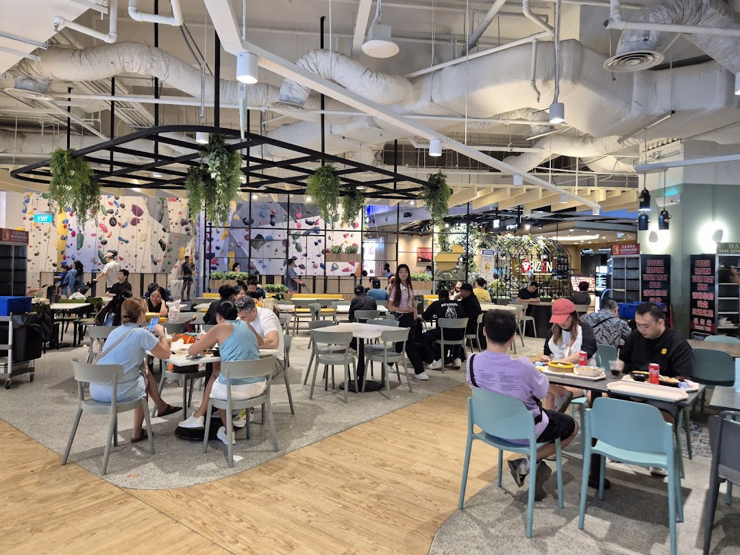 People dining in a spacious food court with a large climbing wall in the background.