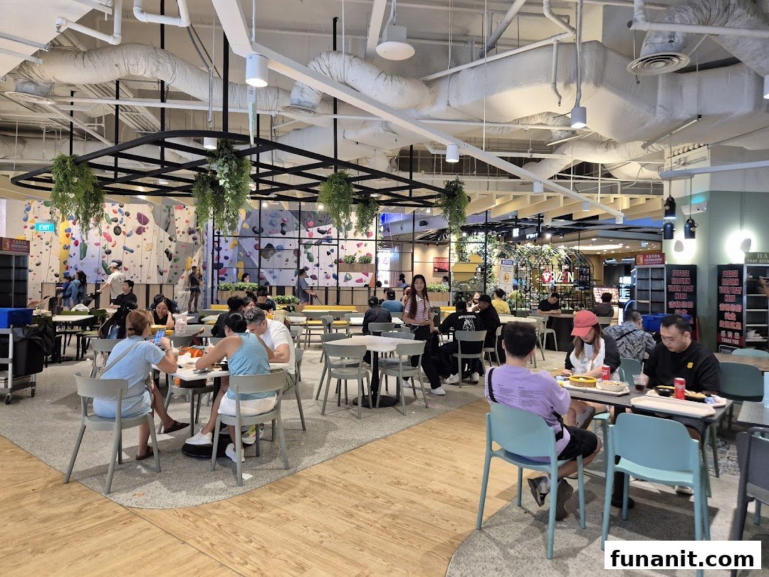 People dining in a spacious food court with a large climbing wall in the background.