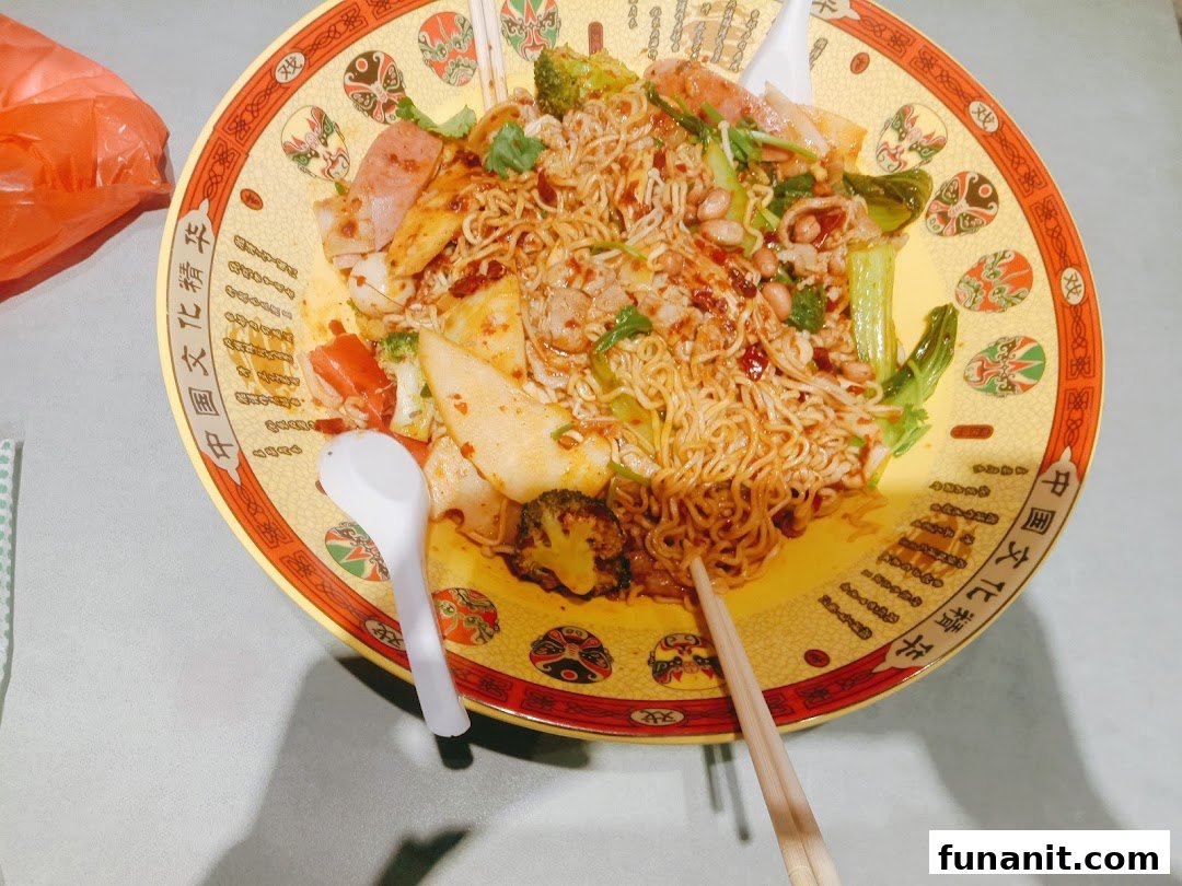 A large, colorful bowl of spicy noodles with various ingredients, served with chopsticks and a spoon.