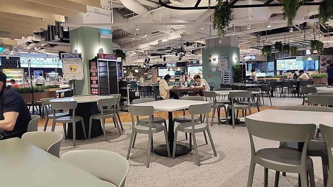 A bustling food court interior with ample seating and various food stalls visible in the background.