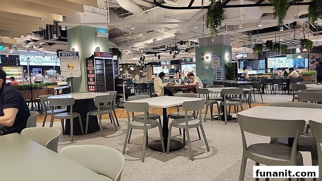 A bustling food court interior with ample seating and various food stalls visible in the background.