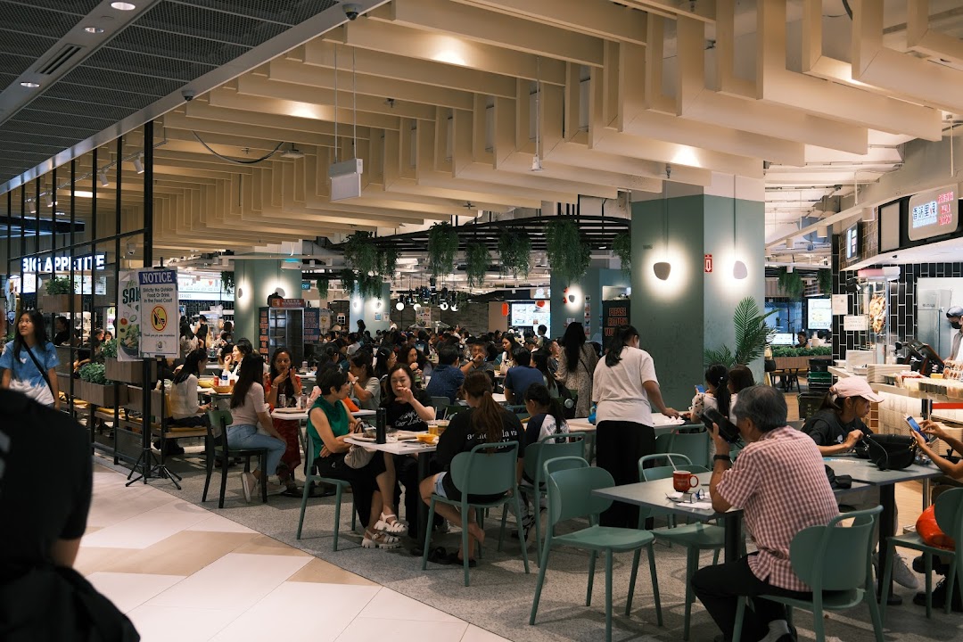 A bustling food court scene with numerous patrons enjoying meals at various tables.
