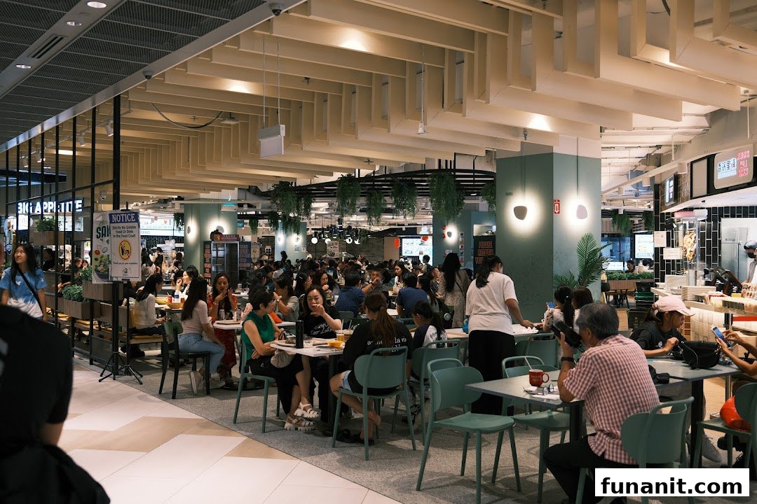 A bustling food court scene with numerous patrons enjoying meals at various tables.