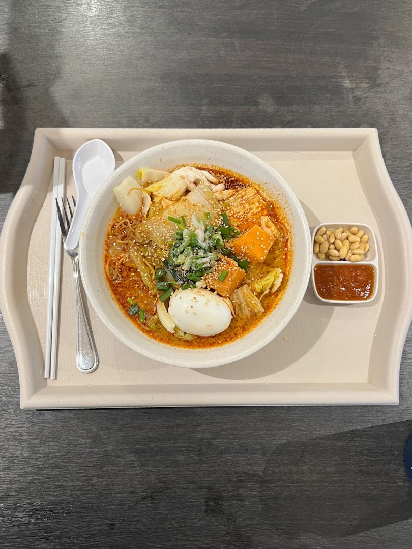 A vibrant bowl of spicy noodles with egg, vegetables, and tofu, served on a tray.