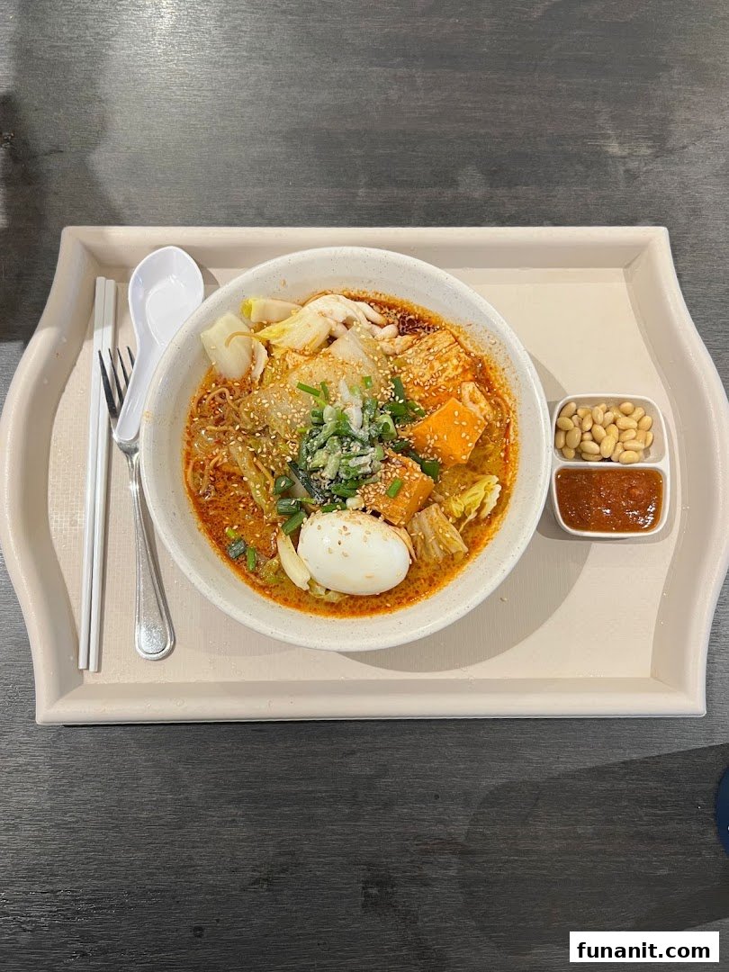 A vibrant bowl of spicy noodles with egg, vegetables, and tofu, served on a tray.