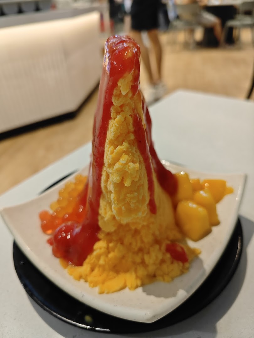 A vibrant mango shaved ice dessert topped with strawberry sauce and fresh mango chunks.