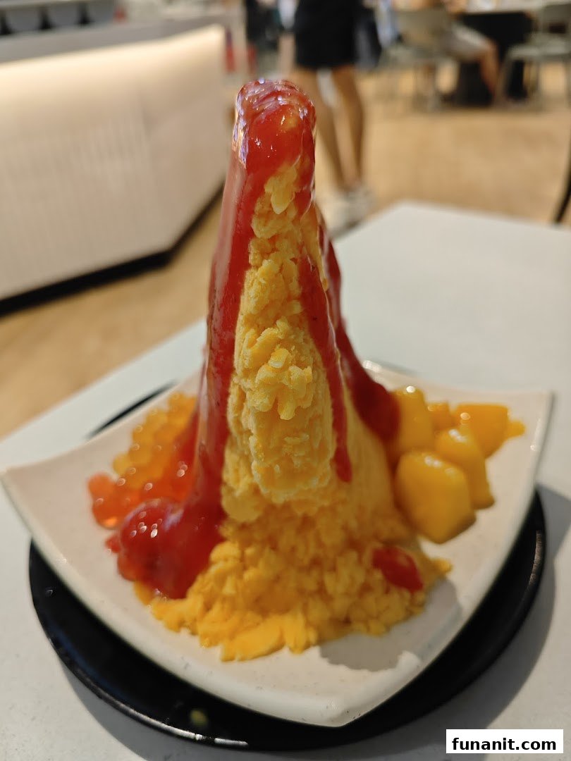 A vibrant mango shaved ice dessert topped with strawberry sauce and fresh mango chunks.