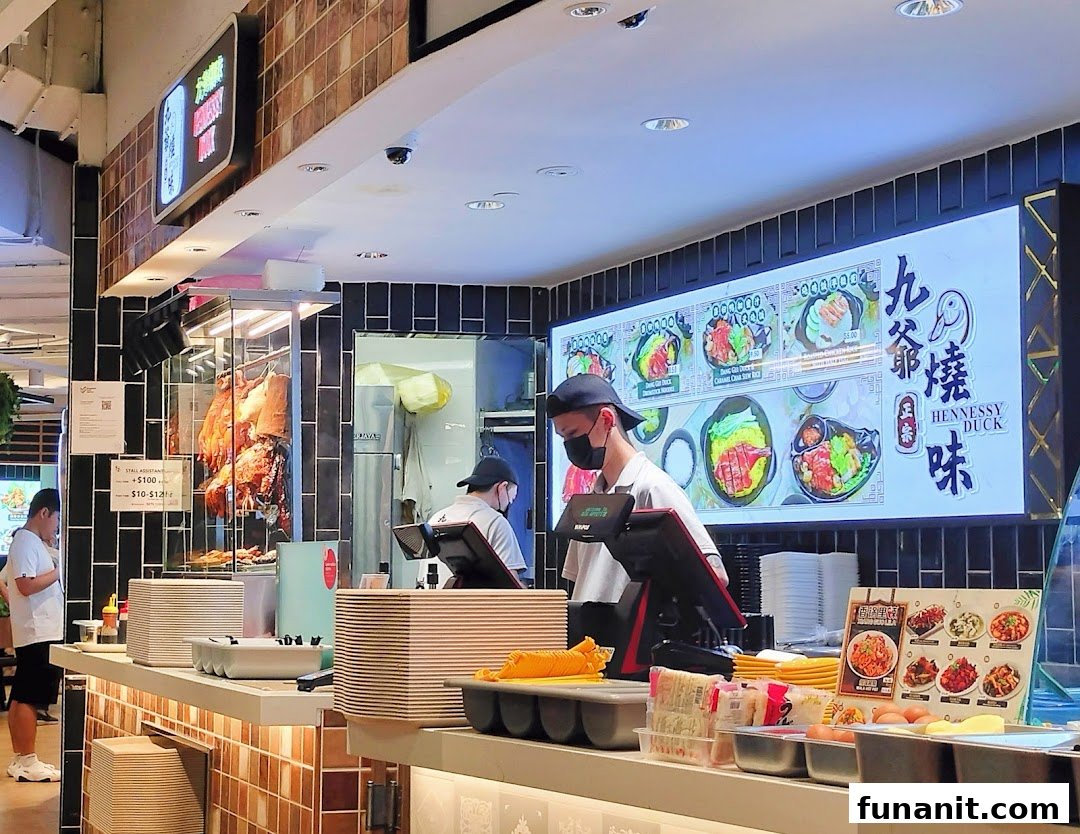 Interior view of a bustling food stall featuring roasted meats, staff, and a digital menu.