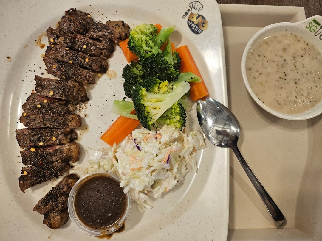 A plate of sliced steak with broccoli, carrots, coleslaw, sauce, and a side of mushroom soup.