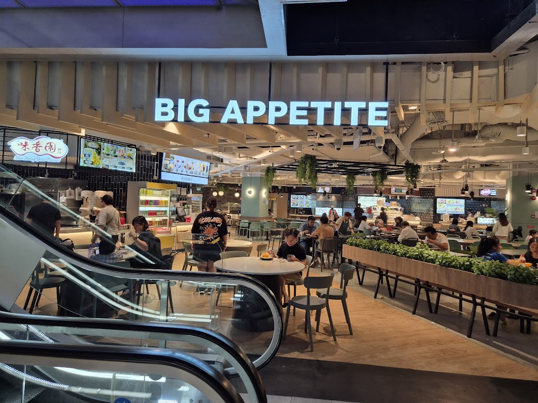 A bustling food court interior with diners, featuring the 'Big Appetite' sign and various food stalls.