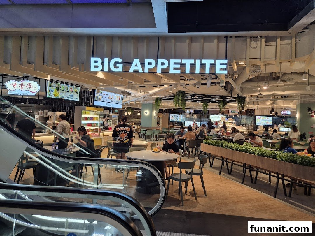 A bustling food court interior with diners, featuring the 'Big Appetite' sign and various food stalls.