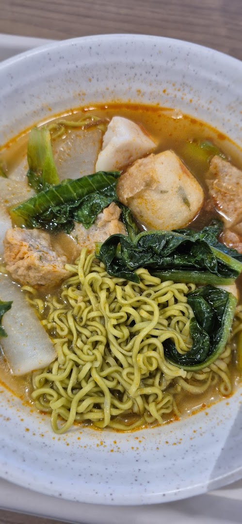A vibrant bowl of green noodles with fish cakes, vegetables, and tofu in a rich broth.