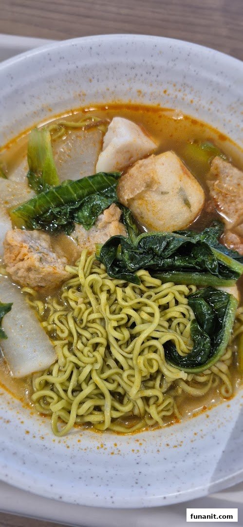 A vibrant bowl of green noodles with fish cakes, vegetables, and tofu in a rich broth.