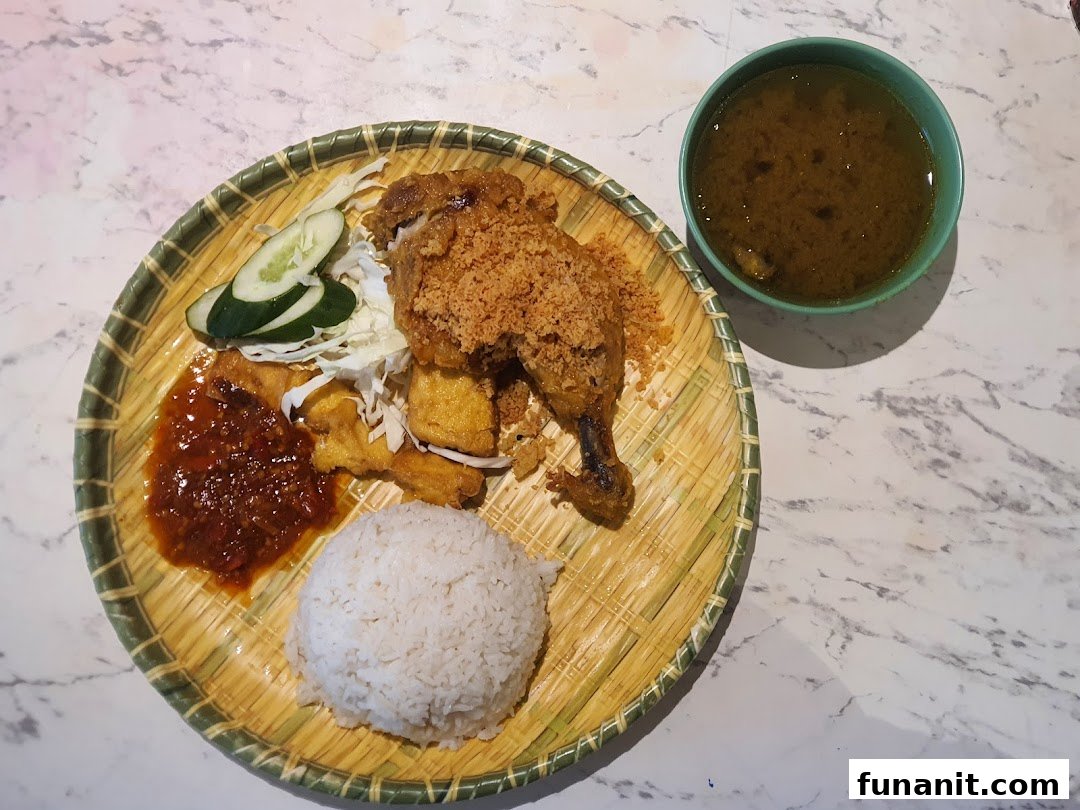 A delicious plate of fried chicken with rice, sambal, and soup, served on a traditional woven plate.