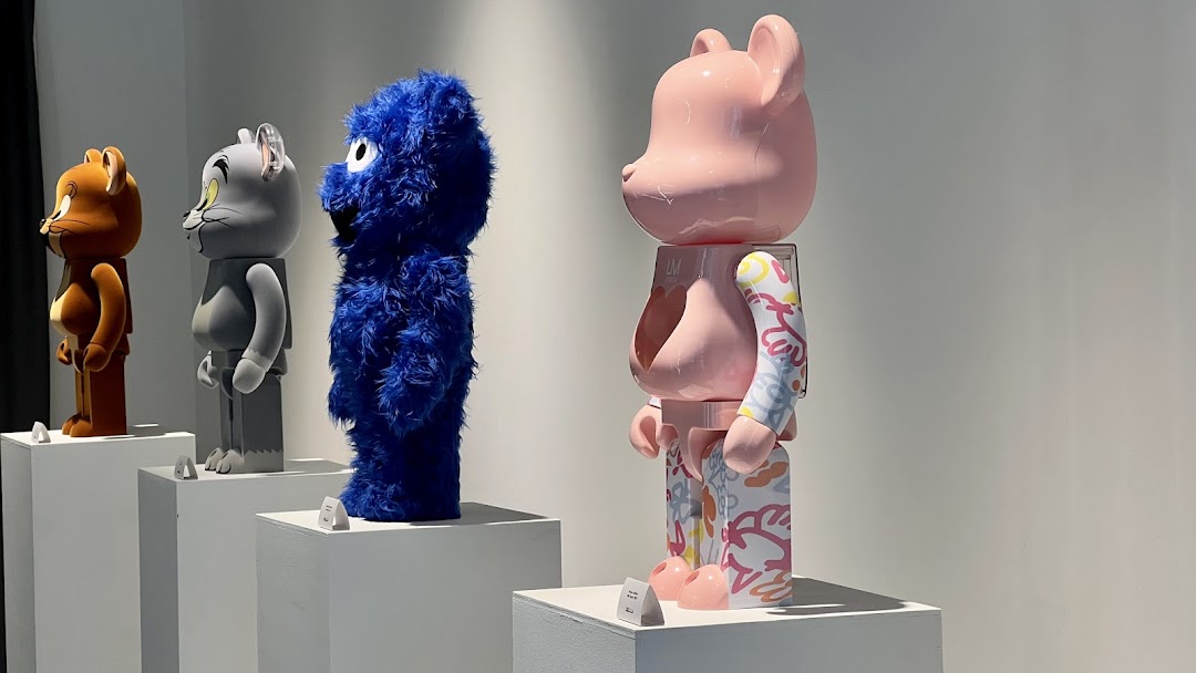 Collectible figures including Tom, Jerry, Cookie Monster, and a Bearbrick displayed in a retail setting.