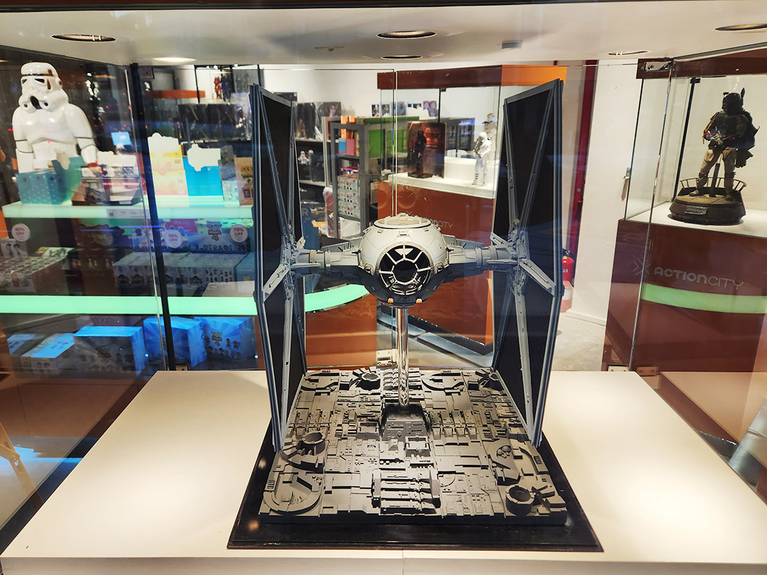 A detailed Star Wars TIE Fighter model is prominently displayed in a shop, surrounded by other pop culture collectibles.