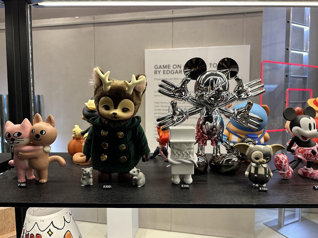 A display of unique collectible art toys, including a chrome Mickey Mouse and other character figures, on a black shelf.