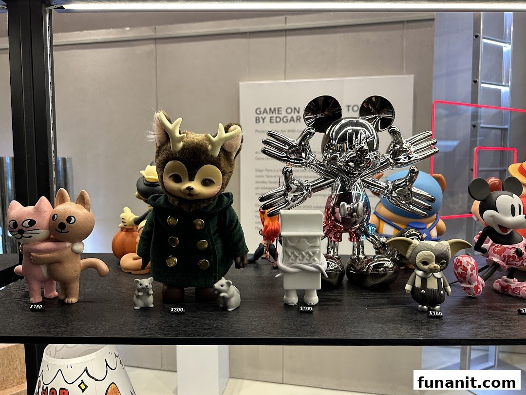 A display of unique collectible art toys, including a chrome Mickey Mouse and other character figures, on a black shelf.