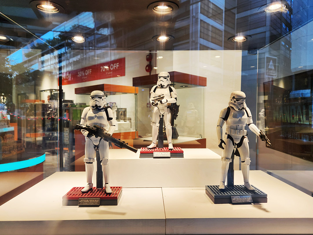 Three Star Wars Stormtrooper figures displayed prominently in a retail shop's front window.