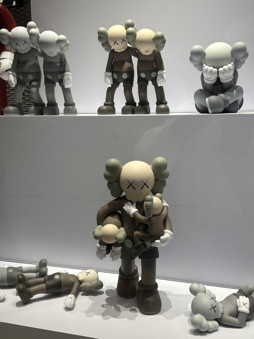 A display of various KAWS Companion art toy figures in different poses and colors on white shelves.