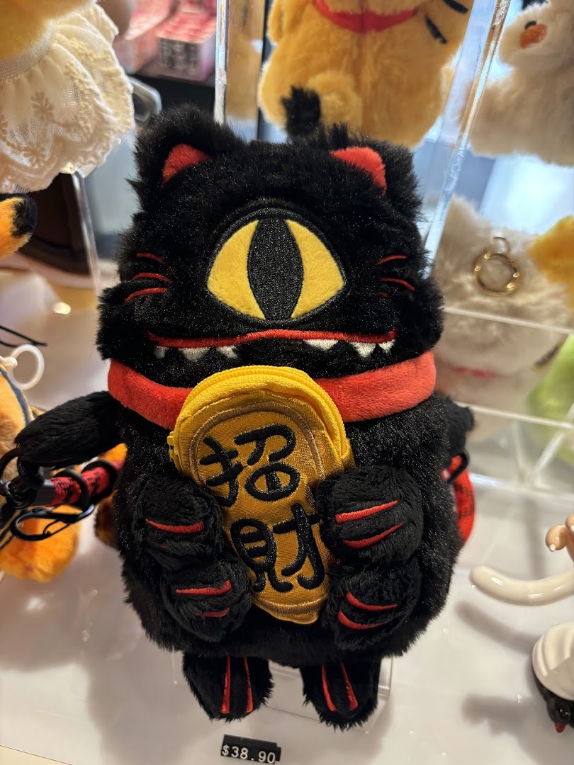 A unique black plush cat toy with a single eye and red accents, holding a golden charm, displayed for sale.