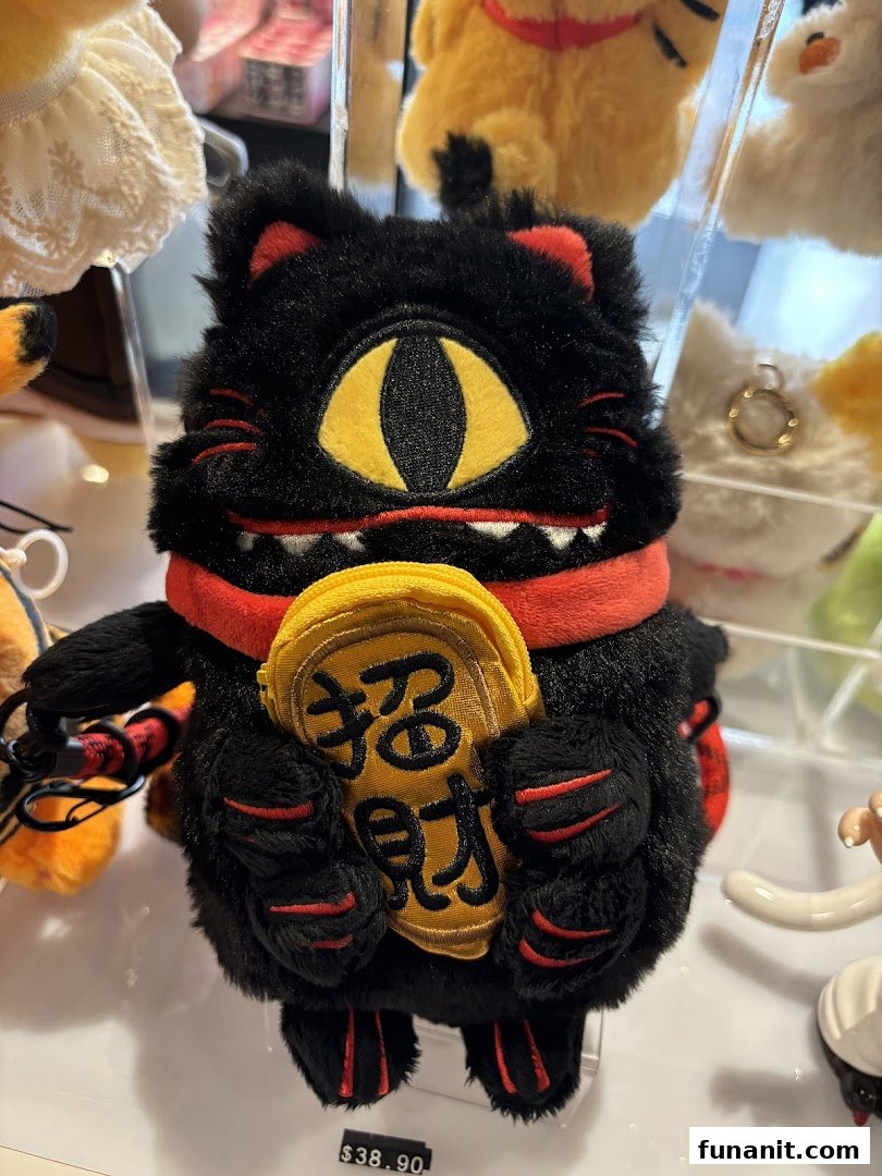 A unique black plush cat toy with a single eye and red accents, holding a golden charm, displayed for sale.