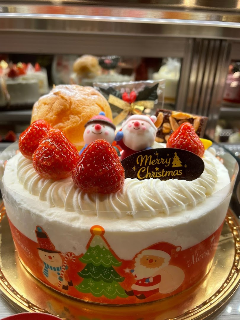 A festive Christmas cake adorned with fresh strawberries, whipped cream, and charming holiday figurines.