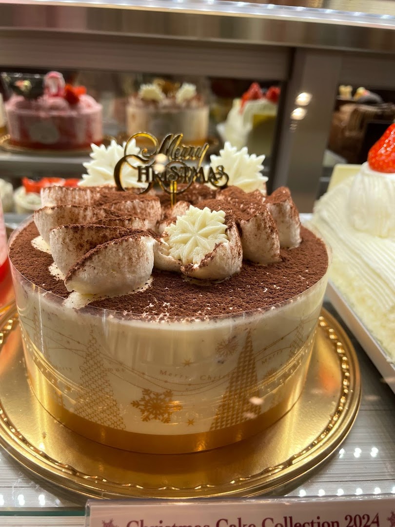 A beautifully decorated Christmas cake with a 'Merry Christmas' topper in a display case.