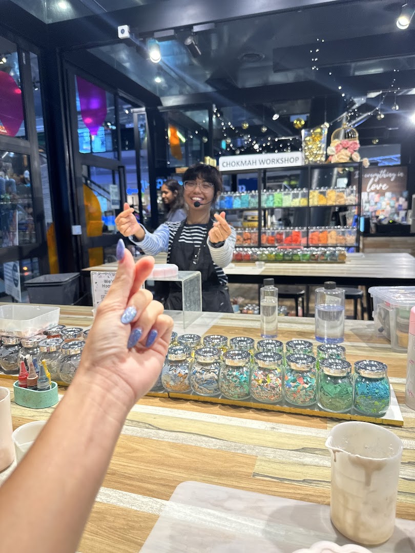 A Chokmah Workshop staff member smiles, making heart gestures amidst colorful craft supplies.