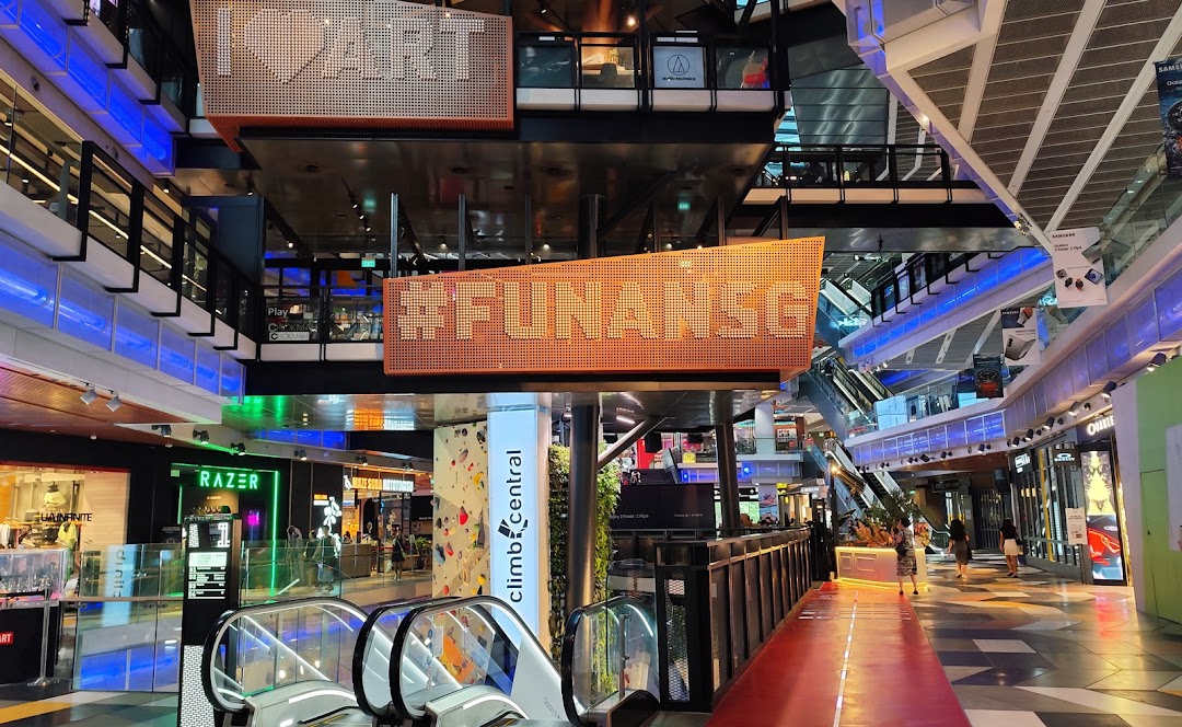 Interior view of Funan mall, showcasing escalators, various shops, and a glimpse of Climb Central's climbing wall.