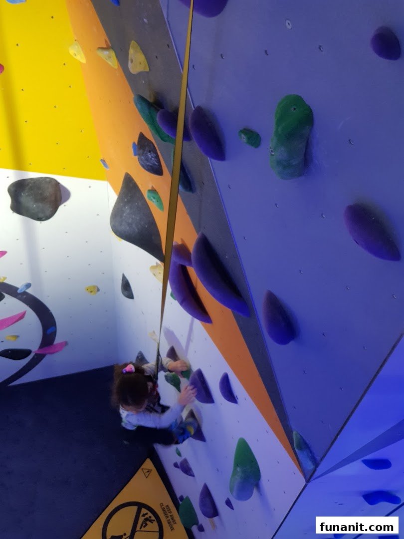 A person is seen actively climbing a vibrant indoor rock wall with various colorful holds.