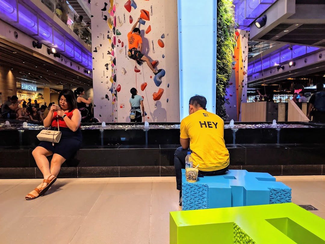 People engaging in indoor rock climbing on a colorful wall at Climb Central Funan, with spectators nearby.