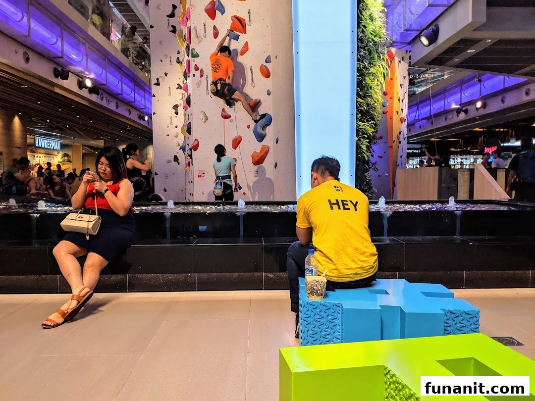 People engaging in indoor rock climbing on a colorful wall at Climb Central Funan, with spectators nearby.