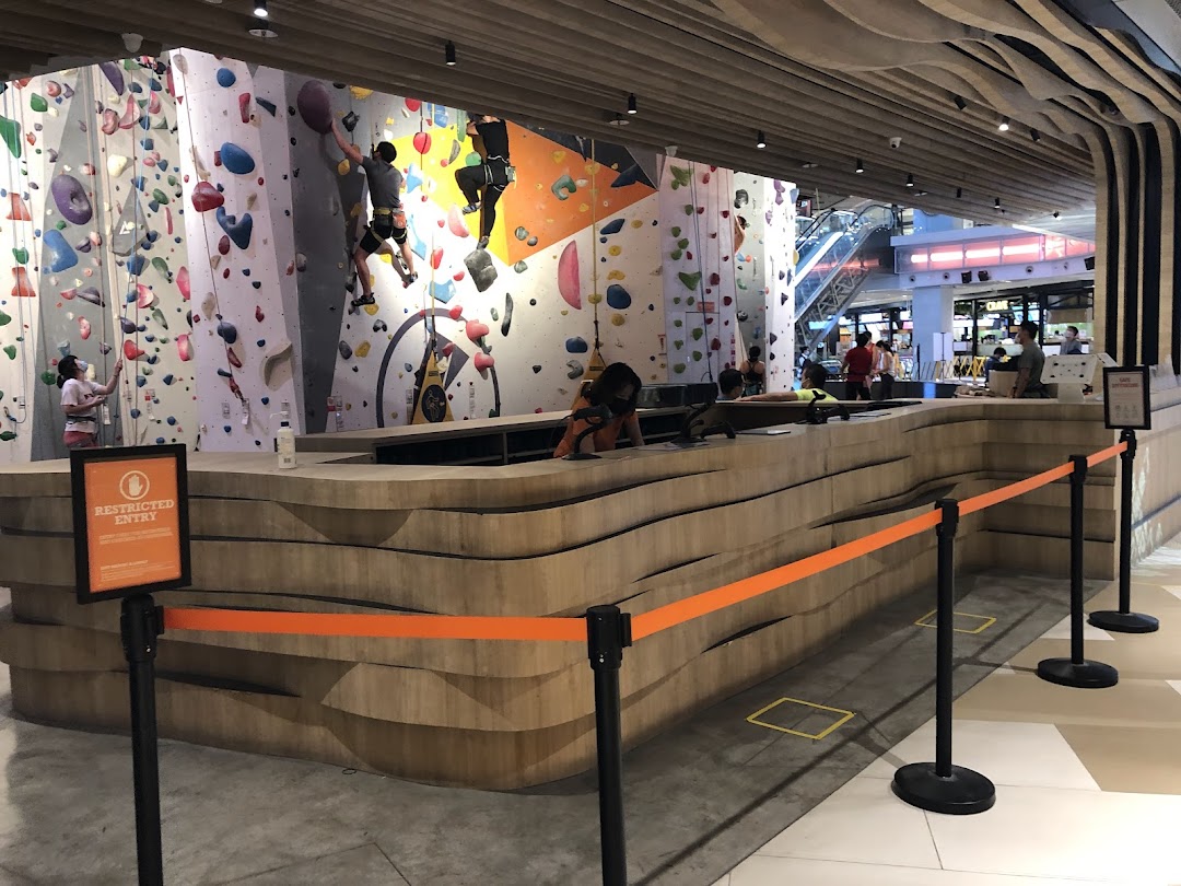 People rock climbing on colorful walls inside Climb Central Funan, with a reception desk in the foreground.