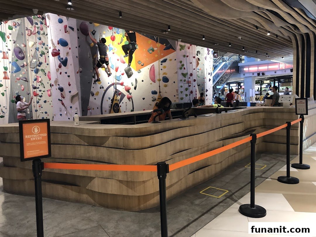 People rock climbing on colorful walls inside Climb Central Funan, with a reception desk in the foreground.