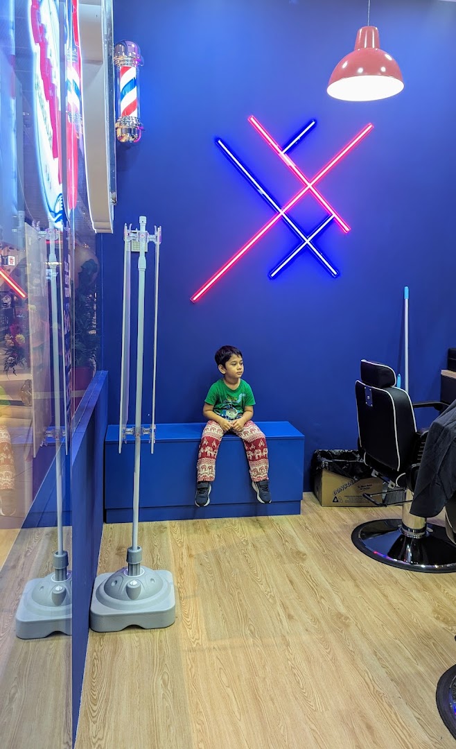 A young boy sits on a blue bench inside Clippers Barber Funan, featuring modern decor and neon lights.