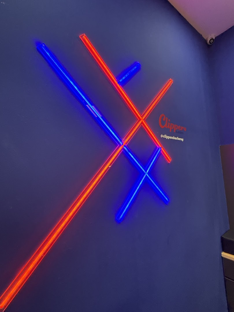 A dark blue wall with red and blue neon lights forming an X and O pattern, featuring the Clippers Barber logo.