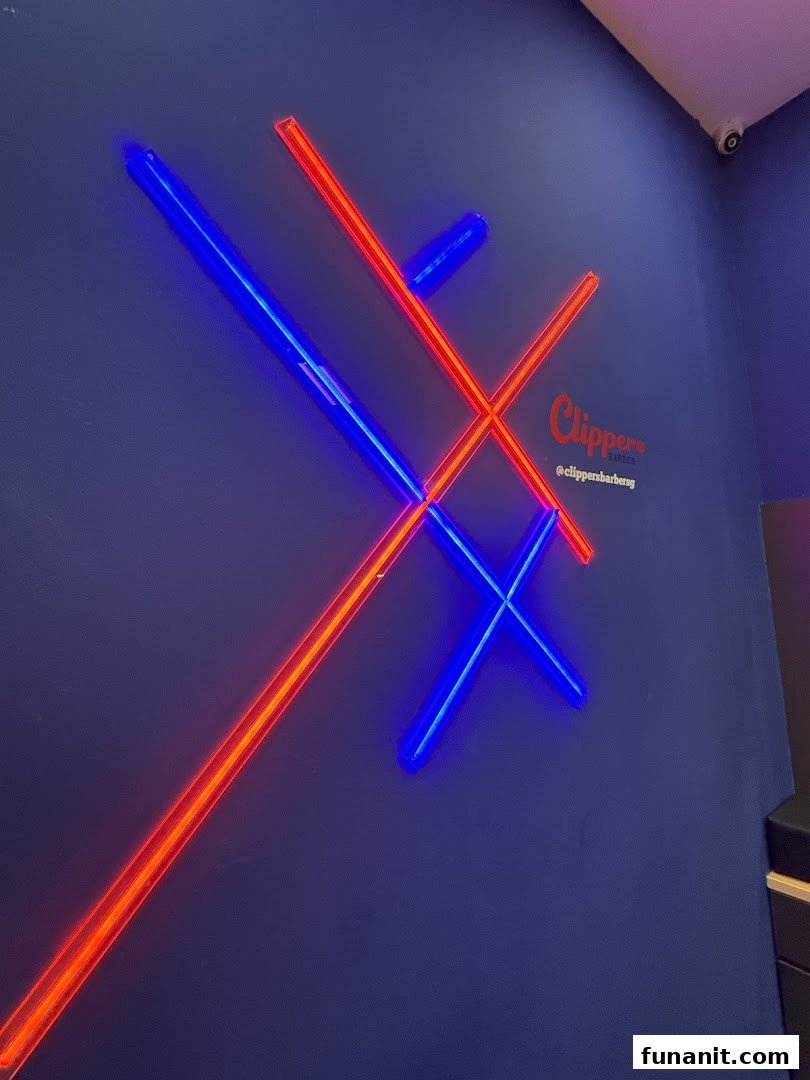 A dark blue wall with red and blue neon lights forming an X and O pattern, featuring the Clippers Barber logo.