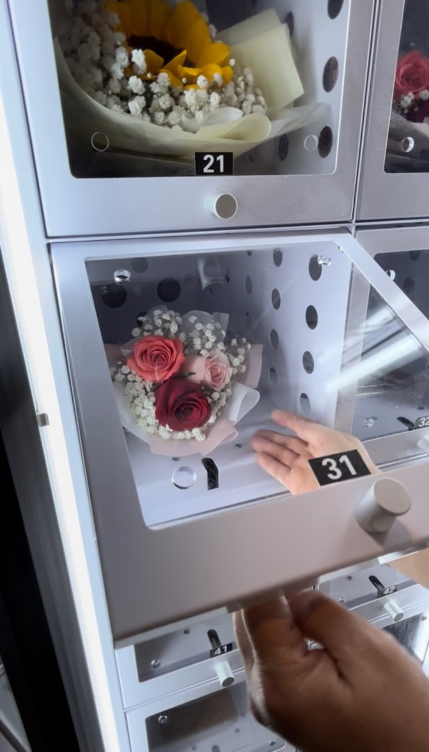 A hand retrieves a beautiful bouquet of roses from a modern flower vending machine.