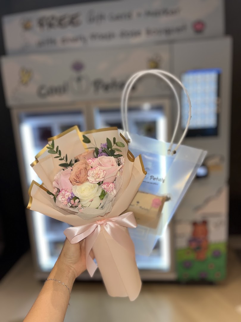 A hand holds a beautiful pink and white flower bouquet in front of a Cool Petals vending machine.