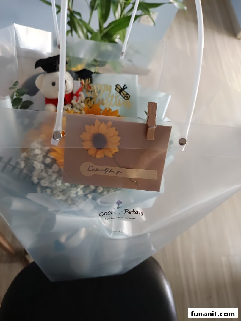 A graduation flower bouquet with sunflowers and a teddy bear in a clear Cool Petals bag.