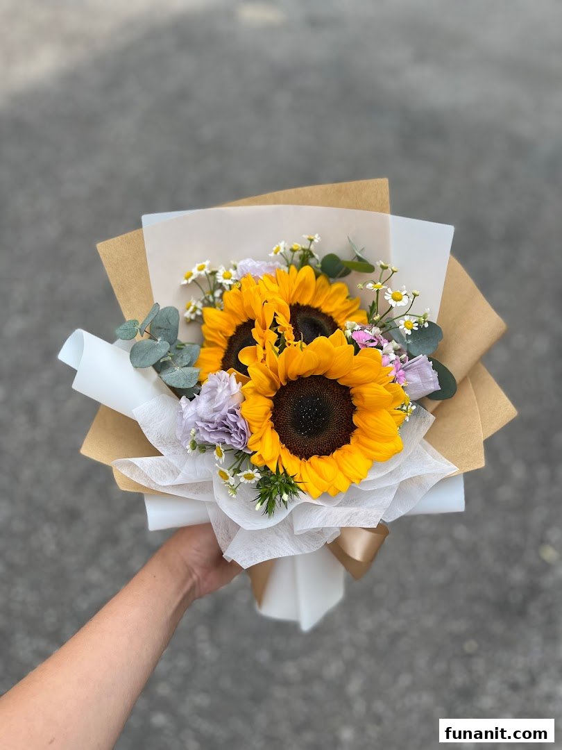 A hand holds a vibrant bouquet of sunflowers, wrapped in brown and white paper.